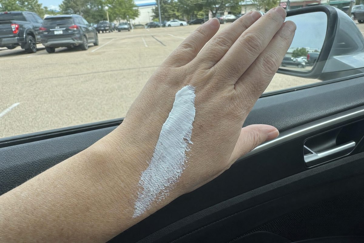 A thick white stripe of mineral sunscreen on the back of a woman's hand, early fifties, beside a car window