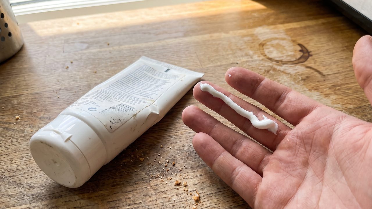 An unlabelled white bottle and a measured line of cream on a fingertip, flat daylight