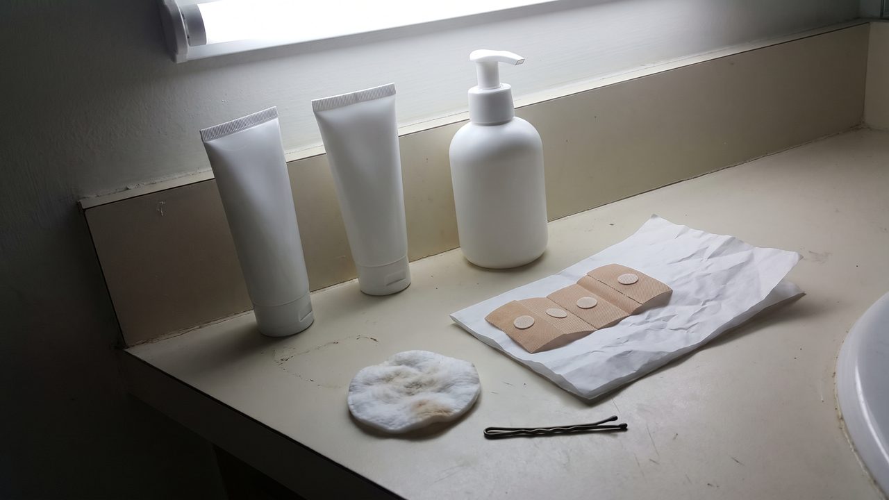 Two plain white tubes and a pump bottle on a bathroom counter next to a strip of patch-test plasters