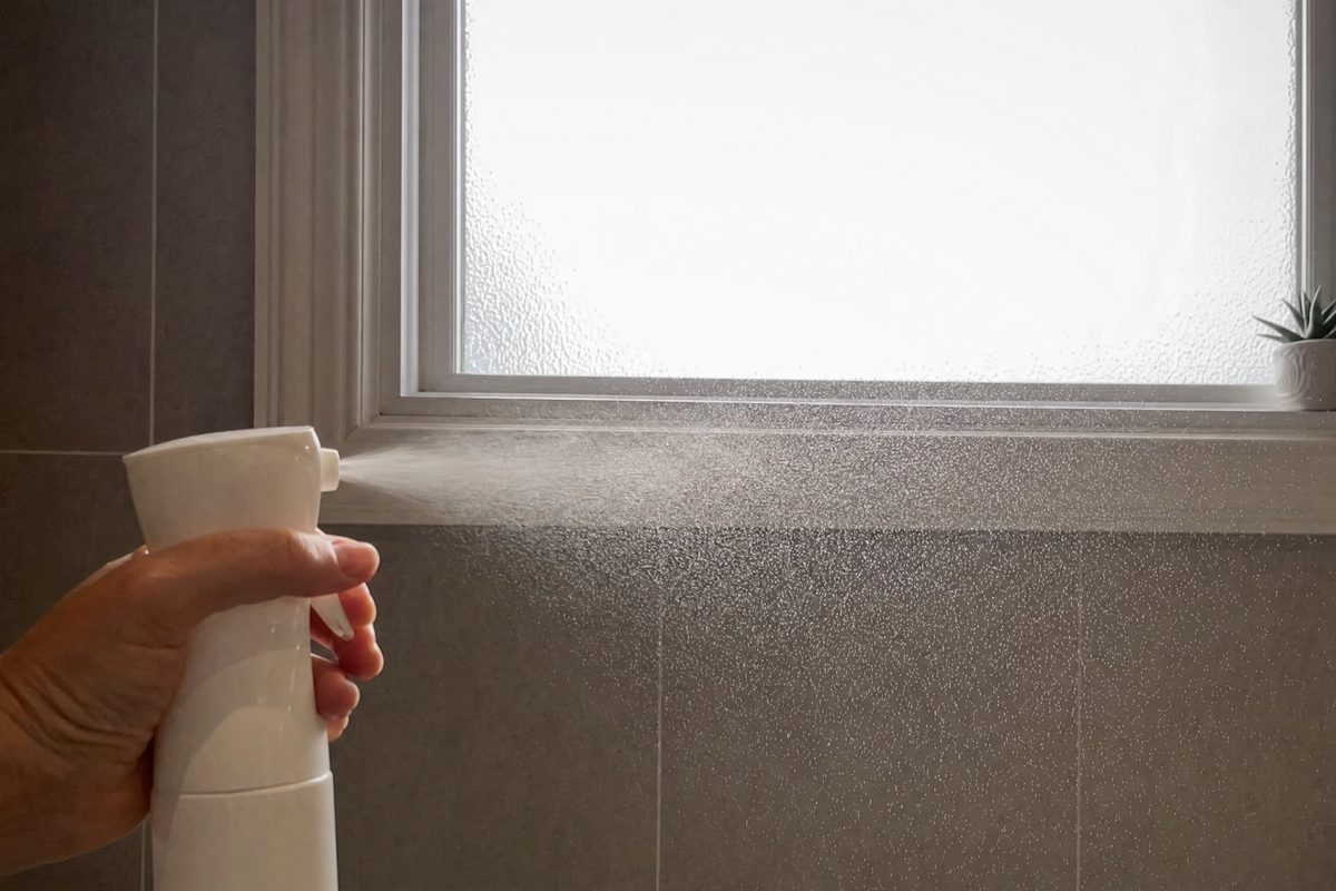 A fine mist from a plain white spray bottle caught in backlight from a bathroom window