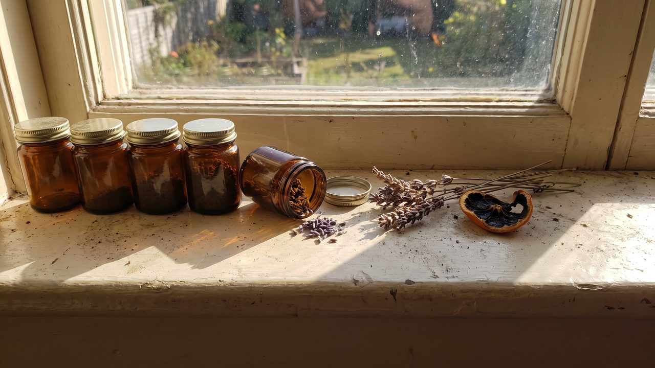 Small dark oil bottles and dried botanicals on a dusty windowsill